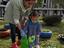 A criança de faixa etária dois anos, com a ajuda da educadora planta alfaces