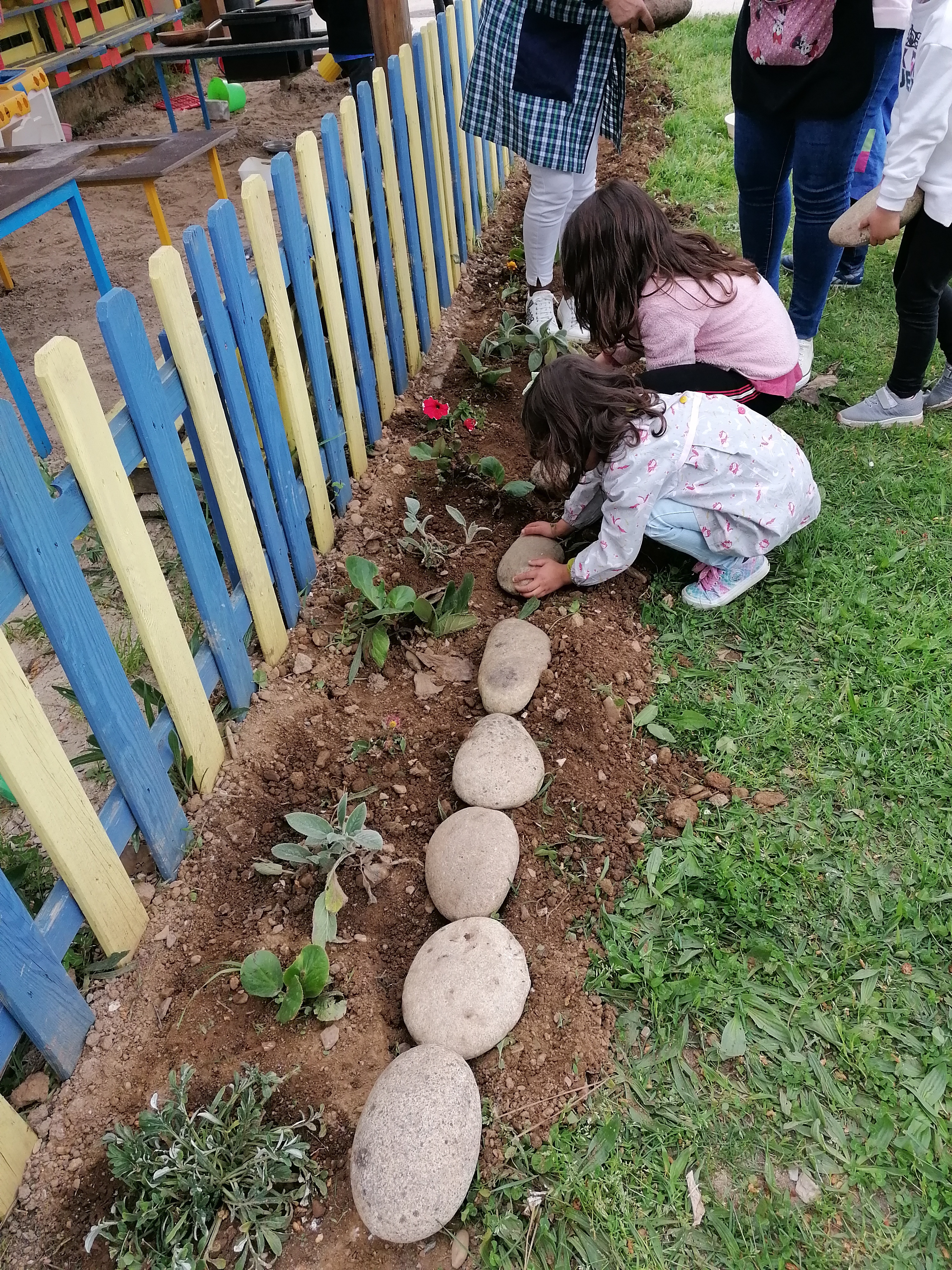 As crianças propuseram limitar o jardim com algumas pedras do lago.