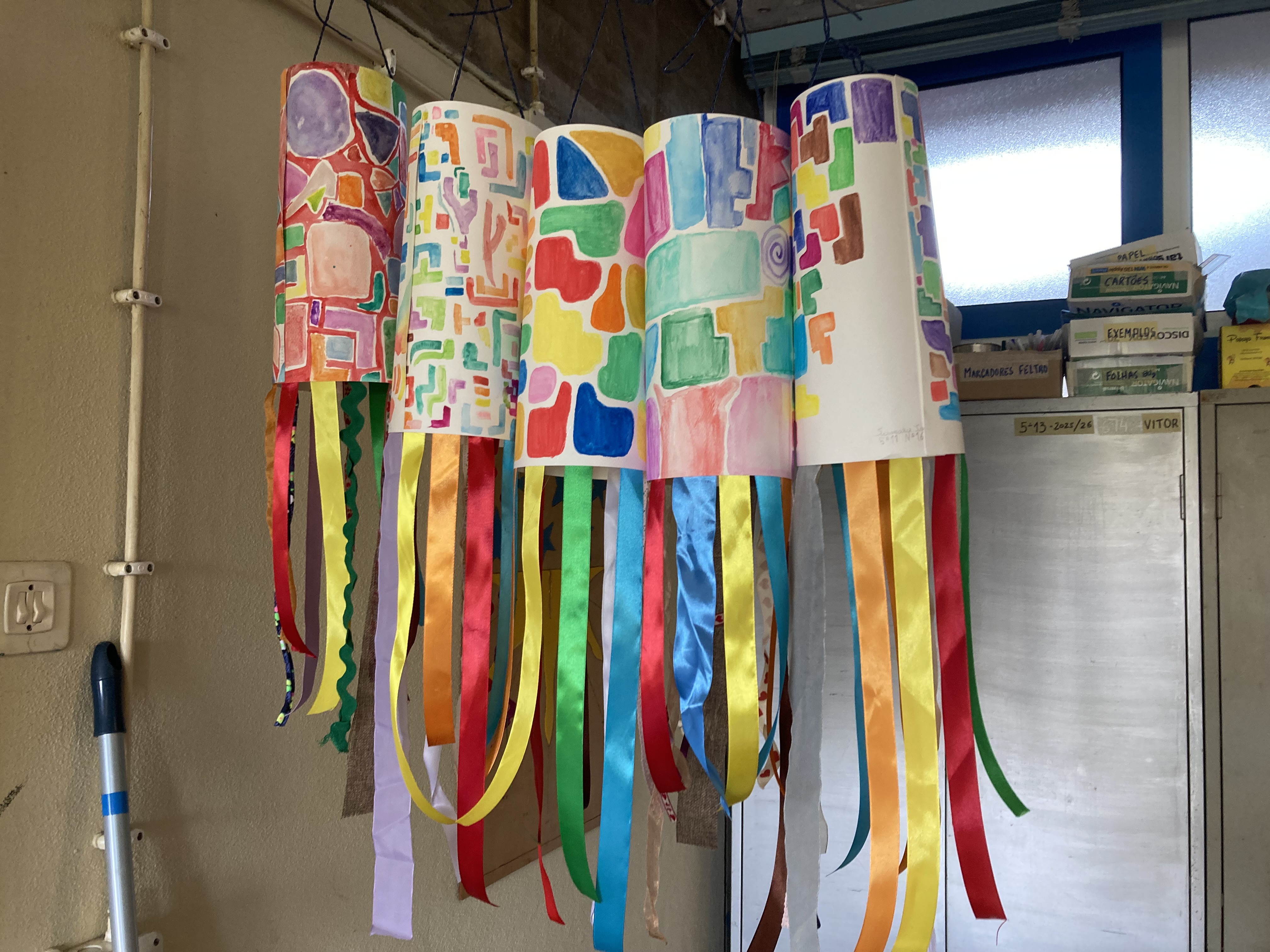 Após a colagem das folhas pintadas e a criação dos candeeiros com efeito cilíndrico, os alunos finalizaram o trabalho acrescentando fitas decorativas. Estas fitas foram colocadas nos candeeiros para dar mais cor, movimento e um efeito visual mais atrativo