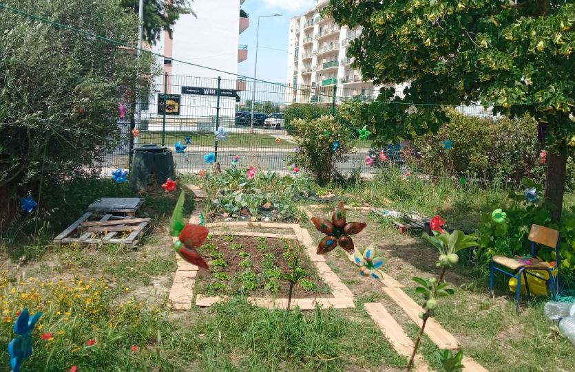 Flores que os alunos fizeram com fundo de garrafa PET e pintaram, penduradas na horta.