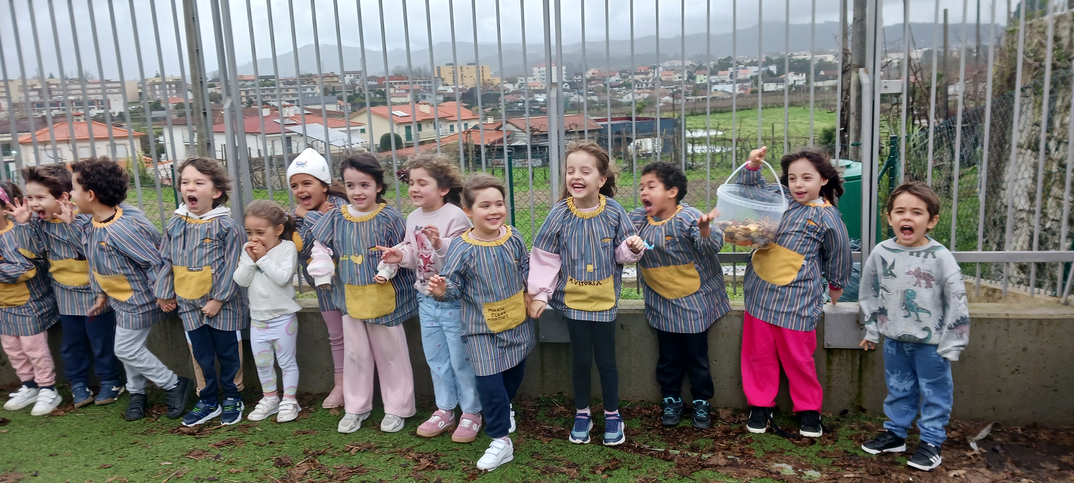 Num dia especialmente chuvoso e ventoso, as crianças aguardam a abertura da porta da horta para colocar o lixo orgânico no compostor.