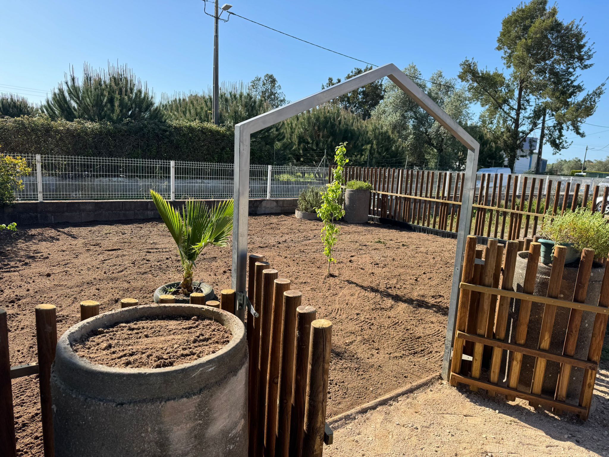Vista da Horta Feliz após a reorganização do espaço, com o terreno preparado, a entrada definida e as primeiras plantas já colocadas. Este momento assinala o (re)começo da horta pronta para ser utilizada em atividades educativas.